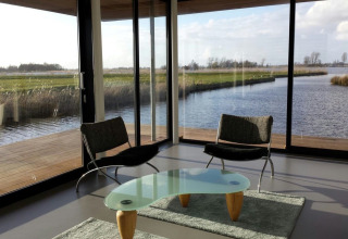 Moderne stue på husbåd Watervilla de Blauwe Reiger med store vinduer og udsigt til vand og natur i Holland.