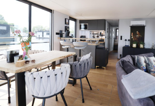 Salón y cocina modernos y luminosos en la casa flotante «Kohlenpott» en Países Bajos, con grandes ventanales.