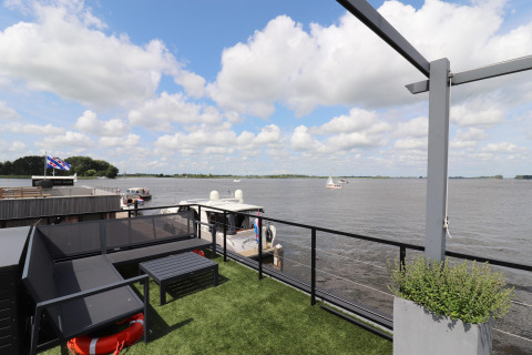 Udsigt fra husbåd Kohlenpott i Holland, med terrasse, sofa og udsigt over floden med både og skyer.
