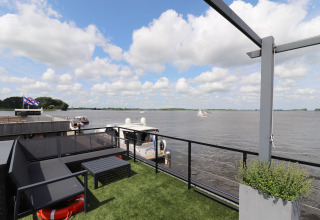 Udsigt fra husbåd Kohlenpott i Holland, med terrasse, sofa og udsigt over floden med både og skyer.