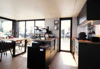 Modernes Wohnzimmer und Küche auf dem Hausboot «Kohlenpott» in den Niederlanden mit großen Fenstern.