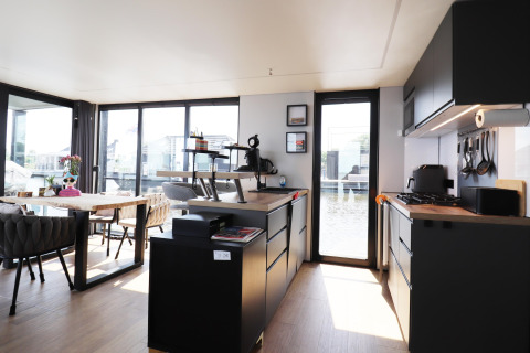 Salón y cocina modernos en la casa flotante «Kohlenpott» en Países Bajos, con ventanales y decoración elegante.