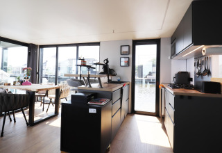 Salón y cocina modernos en la casa flotante «Kohlenpott» en Países Bajos, con ventanales y decoración elegante.