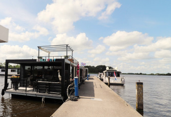 Hausboot „Kohlenpott“ am Steg in den Niederlanden, Boote im Wasser, blauer Himmel und Wolken.