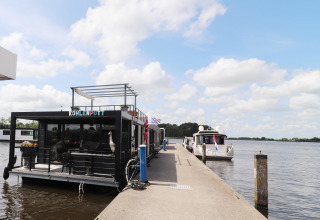Hausboot „Kohlenpott“ am Steg in den Niederlanden, Boote im Wasser, blauer Himmel und Wolken.
