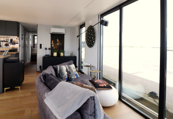 Modernes Wohnzimmer auf Hausboot „Kohlenpott“ in den Niederlanden mit großen Fenstern und Wasserblick.