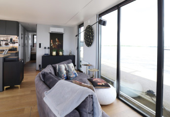 Salon moderne du houseboat «Kohlenpott» aux Pays-Bas avec de grandes fenêtres et vue sur l’eau.