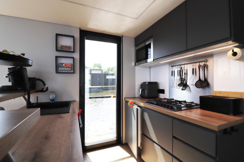 Moderne Küche im Hausboot «Kohlenpott» in den Niederlanden mit Blick über das Wasser durch Glastür.