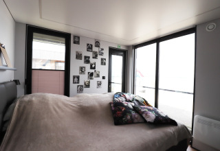 Slaapkamer op woonboot «Kohlenpott» in Nederland met grote ramen en zwart-witfoto’s aan de muur.