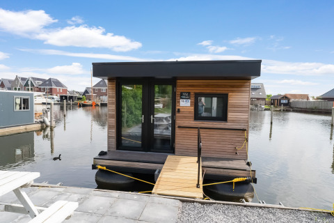 Moderne woonboot Boat House Stavoren, aangemeerd in een haven in Nederland, omringd door huizen.