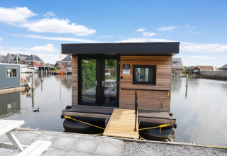 Moderne woonboot Boat House Stavoren, aangemeerd in een haven in Nederland, omringd door huizen.