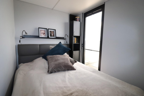 Slaapkamer op woonboot 'Kohlenpott' in Nederland met groot raam, bed, kussens en decoraties.