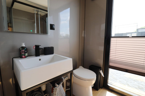 Baño moderno con lavabo, espejo y inodoro en la casa flotante «Kohlenpott» en los Países Bajos, ventana soleada.