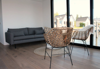 Modernes Wohnzimmer auf einem Hausboot in Stavoren, Niederlande, mit großen Fenstern und Rattanstühlen.