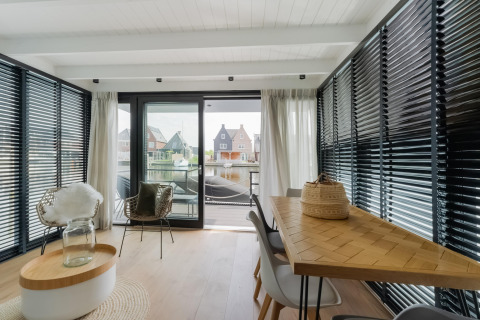 Moderne woonruimte op woonboot in Stavoren met grote ramen, eettafel en uitzicht op het water.