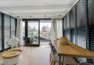Moderne woonruimte op woonboot in Stavoren met grote ramen, eettafel en uitzicht op het water.