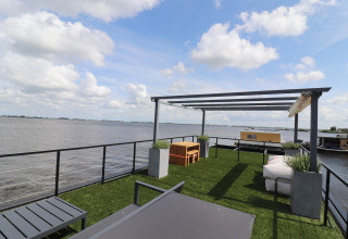 Terraza superior de la casa flotante «Kohlenpott» en Países Bajos, con césped sintético y vistas al agua.
