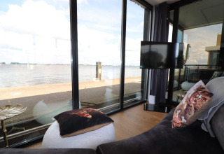 Lichte woonkamer op woonboot «Kohlenpott» met grote ramen en zicht op het water in Nederland.