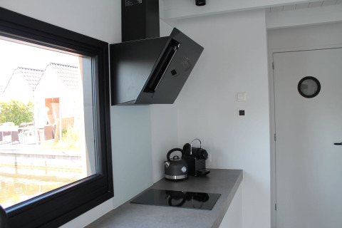 Moderne keuken op een woonboot in Stavoren met inductiekookplaat, waterkoker en uitzicht op het water.