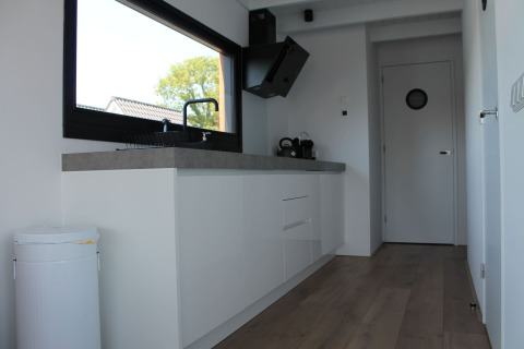 Moderne keukeninterieur op een woonboot met groot raam, witte kasten en houten vloer in Stavoren, Nederland.