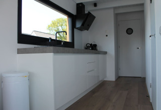 Moderne keukeninterieur op een woonboot met groot raam, witte kasten en houten vloer in Stavoren, Nederland.