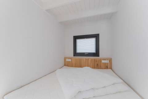 Kleine minimalistische slaapkamer met houten hoofdbord, wit beddengoed en raam in Boat House Stavoren.