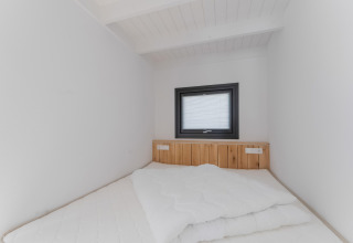 Kleine minimalistische slaapkamer met houten hoofdbord, wit beddengoed en raam in Boat House Stavoren.