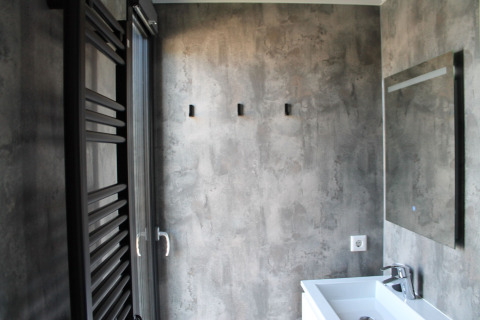 Moderne badkamer op een woonboot met betonlook muren, spiegel, witte wastafel en handdoekradiator.