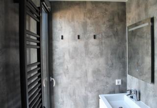 Moderne badkamer op een woonboot met betonlook muren, spiegel, witte wastafel en handdoekradiator.