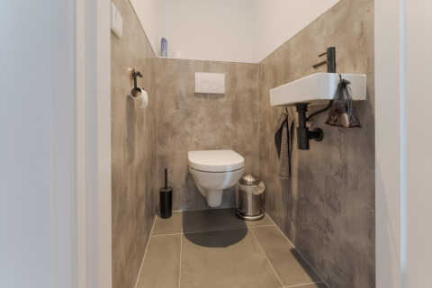 Modern toilet met hangend closet, kleine wastafel en grijze tegels in Boat House Stavoren, Nederland.