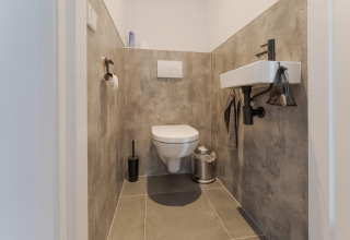 Modern toilet met hangend closet, kleine wastafel en grijze tegels in Boat House Stavoren, Nederland.