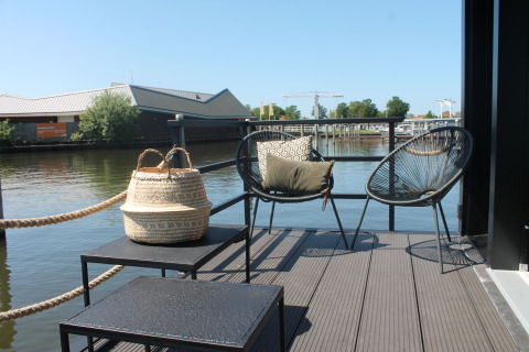 Buitenterras van woonboot Boat House Stavoren in Nederland met stoelen, tafels en uitzicht op water.