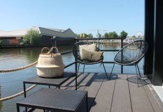 Buitenterras van woonboot Boat House Stavoren in Nederland met stoelen, tafels en uitzicht op water.