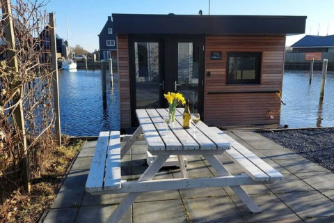 Witte picknicktafel met bloemen voor woonboot «Boat House Stavoren» aan het water in Nederland.