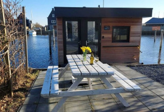 Witte picknicktafel met bloemen voor woonboot «Boat House Stavoren» aan het water in Nederland.