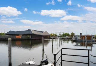 Uitzicht vanaf woonboot Boat House Stavoren in Nederland met steiger, boten en modern gebouw.