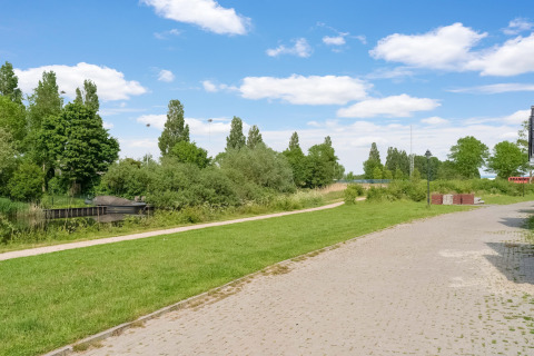 Uitzicht op pad, grasveld en water bij Boat House Stavoren in Nederland, met groene bomen en blauwe lucht.