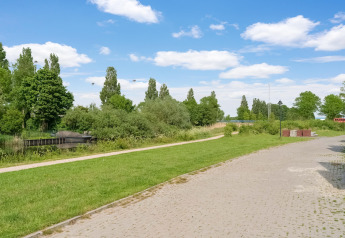Blick auf einen Weg, Rasen und Wasser am Boat House Stavoren, Niederlande, mit vielen grünen Bäumen.