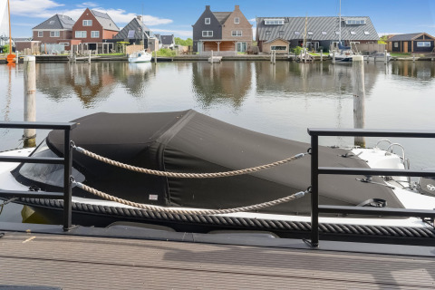 Afgedekte boot aan de steiger voor moderne huizen in Stavoren, Nederland, gezien vanaf een woonboot.