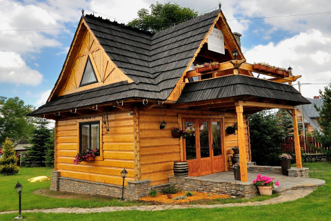 Knus houten chalet met zwart dak, balkon en bloempotten in een groene tuin in de Tsjechische bergen.