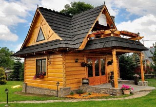 Knus houten chalet met zwart dak, balkon en bloempotten in een groene tuin in de Tsjechische bergen.