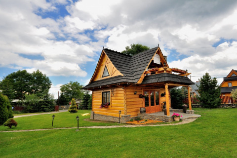 Knus houten chalet met zwart dak in een groene tuin, omgeven door een prachtig berglandschap.