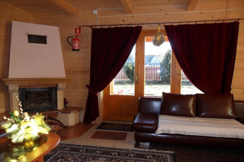 Gezellige woonkamer in een chalet in Tsjechië met open haard, rode gordijnen en leren bank.