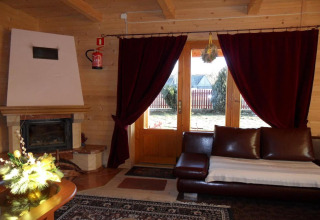 Knusse chaletwoonkamer in Tsjechië met haard, bordeaux gordijnen en leren zetel, uitzicht op tuin.