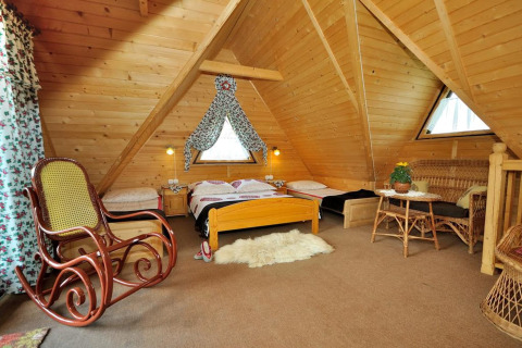 Gezellige zolderkamer met houten structure, schommelstoel, bedden en rieten meubels in een bergchalet.