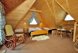 Gezellige zolderkamer met houten structure, schommelstoel, bedden en rieten meubels in een bergchalet.