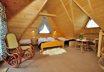 Chambre mansardée chaleureuse en bois avec fauteuil à bascule, lits et meubles en osier dans un chalet.