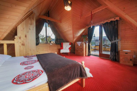 Gezellige chalet slaapkamer met houten plafond, rood tapijt en balkon in de Tsjechische bergen.