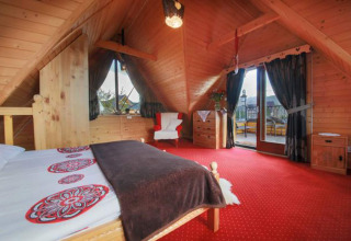 Gezellige chalet slaapkamer met houten plafond, rood tapijt en balkon in de Tsjechische bergen.