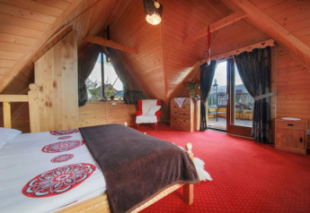 Camera da letto in chalet con soffitto in legno, moquette rossa e balcone nelle montagne ceche.